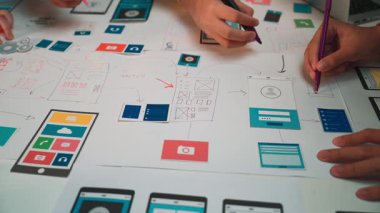 A creative workspace features hands collaborating on colorful mobile app wireframes and sketches, showcasing the design process and teamwork in a digital atmosphere. SACTR