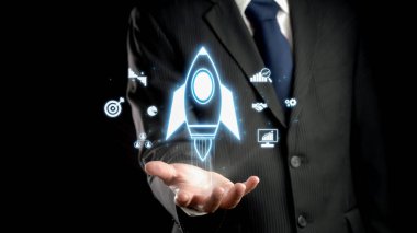 A businessman in a suit showcases a rocket icon alongside digital marketing symbols, symbolizing growth and innovation in a professional setting against a dark background. Qubit
