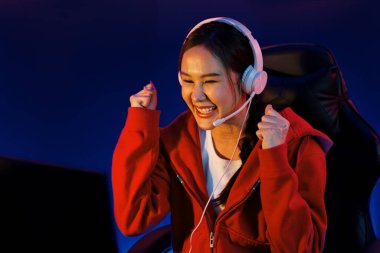 Yüzünde kulaklık renginde kulaklık takan, neon odada online oyun oynayan, Esport meziyetli takım oyuncularına yumruk kaldırarak oynayan güzel Asyalı kız flamasının sunucu kanalı. Taktik.