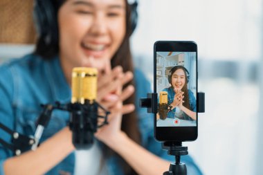 Asyalı sunucu canlı yayında canlı yayında canlı yayında sosyal medyada kulaklık takarak konuşuyor. Dinleyicileri modern stüdyoda koçluk yaparak selamlıyor. Taktik.