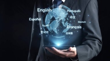 A businessman in a professional suit holds a smartphone displaying a virtual globe with various language names, symbolizing global communication and connectivity. Qubit