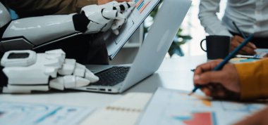 İnsanlarla işbirliği yapan bir robotu gösteren dinamik bir ofis sahnesi, dizüstü bilgisayar ve çizelgeler, teknolojinin modern iş uygulamalarıyla bütünleşmesini gösteriyor. Noogenesis