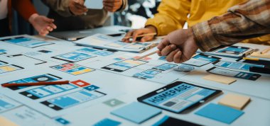 Çeşitli bir ekip bir beyin fırtınası oturumunda işbirliği yapar, kablo çerçeveleri oluşturur ve çizimler ve notlarla dolu bir masada bir uygulama tasarımı için yenilikçi fikirleri tartışır. SACTR