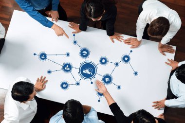 A top-down view of a team collaborating on business strategies with various icons symbolizing communication, technology, and growth in a modern office setting. Amity