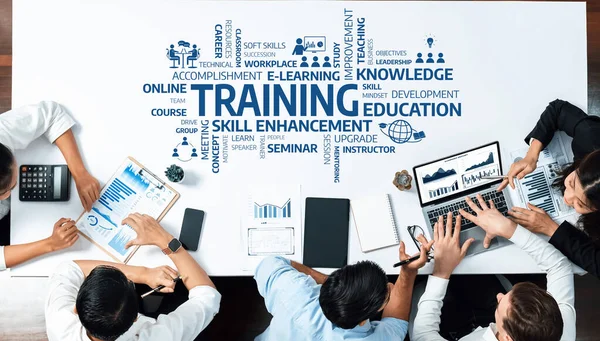 A diverse group of professionals collaborates in an e-learning training session, using laptops and data charts to enhance their skills and develop knowledge in a modern workspace. Amity