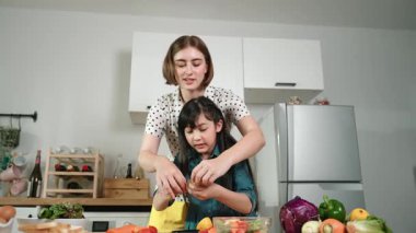 Zeki beyaz anne ve Asyalı kız birlikte yemek pişiriyor ve sebze doğruyor ya da akşam yemeği için salata hazırlıyor. Mutlu anne ve kız taze yemekle sağlıklı yemek yapıyorlar. Eğitim konsepti. Pedagoji.