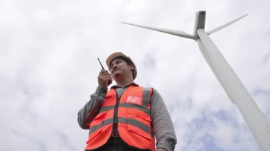 Gökyüzü arka planına sahip bir rüzgar türbini üzerinde çalışan mühendis. Yenilenebilir ve sürdürülebilir enerjinin gelecekteki üretimi için yenilikçi bir ideal. Rüzgar türbininden enerji üretimi.