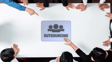A diverse business team collaborates on an outsourcing strategy in a modern conference room, using digital icons to represent various planning aspects. Raster
