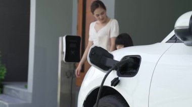 Evde şarj edilen elektrikli bir araçla okuldan yeni dönen anne ve kızın ilerici yaşam tarzı. Elektrikli araç, sürdürülebilir temiz enerjiyle çalışıyor..