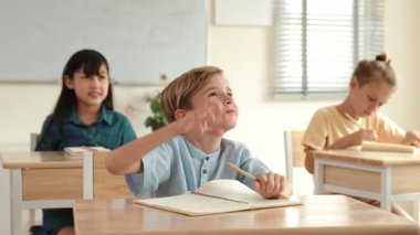 Kafkasyalı zeki çocuk, ilkokulda öğretmenlerin geçişi sırasında sınıfta okuyan çeşitli çocuklarla çevrili öğretmenlere sorduğu ve cevap verdiği için elini kaldırıyor. Eğitim konsepti. Pedagoji.