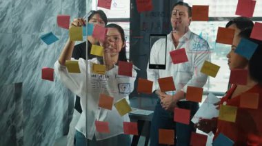 Cam duvarda yaratıcı fikirleri paylaşmak için renkli yapışkan notlar kullanarak pazarlama fikrini değerlendiren mutlu profesyonel iş adamları. Bir grup farklı iş adamları strateji hakkında tartışıyorlar. Yönlendirici.