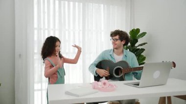 Çekici beyaz bir baba gitar çalarken tatlı bir kız müzik eşliğinde dans ediyor. Mutlu baba ve Amerikalı kız birlikte vakit geçirirken akıllı çocuk müzik yapıyor. Aile eğlence konsepti. Pedagoji.