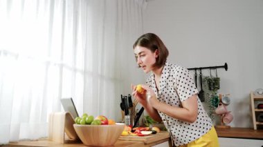 Kafkasyalı anne, modern mutfakta dizüstü bilgisayarda yemek tarifine bakarken salata yapmak için yemek hazırlıyor. Yetenekli ev bekçisi taze sebze kullanarak kahvaltı hazırlıyor. Pedagoji.