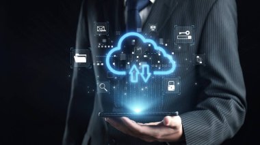 A businessman in a formal suit holds a tablet with an illuminated cloud technology concept, showcasing various digital icons and data exchange elements against a dark backdrop. Qubit