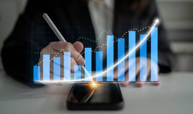 A business professional engages in financial analysis using a smartphone and digital chart, emphasizing growth trends and strategic planning in a modern workspace. Impute