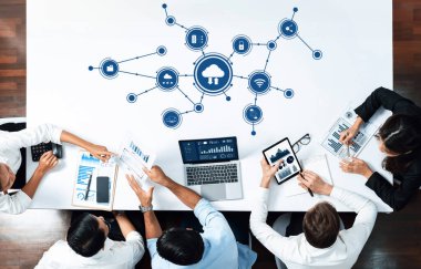 A top-down view of a business team collaborating on cloud computing strategies, using laptops and charts to analyze data and discuss innovative solutions. Amity