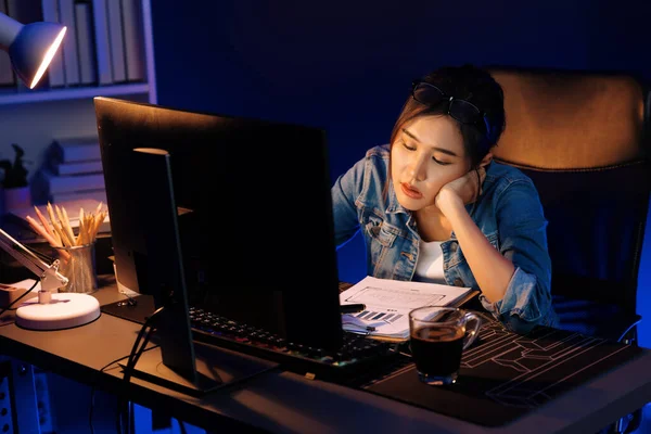 Stresli, genç, güzel Asyalı yaratıcı proje yaratıcısı sosyal medyayı araştırmak için bilgisayara bakıyor ve geceleri daha çok neon modern ofisin planlama kanalı stratejisine ulaşılıyor. Taktik.