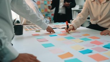 A diverse group of professionals engages in an interactive brainstorming session using colorful sticky notes in a modern office setting, promoting teamwork and creativity. SACTR