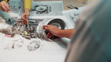 A group of engineers engaged in a collaborative session on turbine engine design, surrounded by detailed technical drawings and blueprints in a modern workspace. SACTR