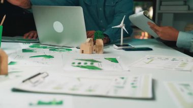 Professionals engage in a collaborative session, analyzing data and discussing sustainable solutions. A wind turbine model adds a creative touch to their innovative workspace. SACTR
