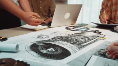 A modern team engages in a collaborative meeting over detailed technical drawings and a laptop in a bright office, exploring innovative engineering concepts and designs. SACTR