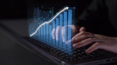 A close-up of hands typing on a laptop, featuring a digital financial graph overlay that illustrates business growth and data analytics in a modern workspace. Copula