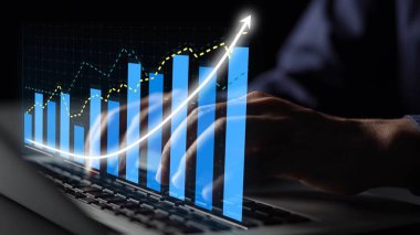 A close-up of a person hands typing on a laptop, showcasing a digital display of financial growth metrics and chart data, symbolizing business success and analysis. Copula