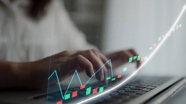 A close-up view of hands typing on a laptop, complemented by a digital graph overlay showing financial growth and market trends in a modern workspace environment. Copula