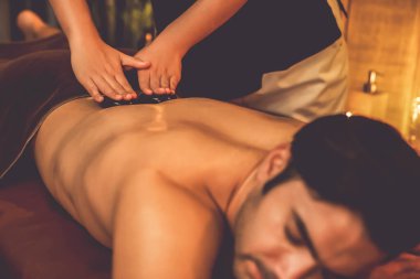 Sıcak mum ışığıyla lüks bir tatil köyündeki kaplıca salonunda sıcak taş masajı, mutlu erkek müşteri bazalt taşı masajının keyfini çıkarırken rahatlatıcı bir sıcaklıkla vücudun üzerinde süzülüyor. Sessiz.