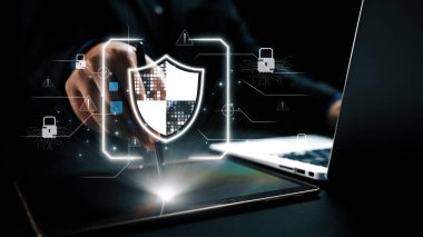 Bir iş adamı, çağdaş bir ofis ortamında modern teknoloji ve veri korumasını gösteren bir siber güvenlik kalkanını görselleştirmek için bir tabletle etkileşime girer. Dörtgen