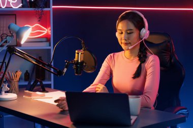 Geceleri podcast 'te olumlu konuşmalar yapan, pembe neon ışıklı modern stüdyoda sunum için dizüstü bilgisayar kullanan, gülümseyen, genç, güzel Asyalı bir etkileyiciydi. Taktik.