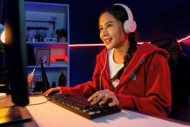 İnternet üzerinden kulaklık takıp gülümseyen Asyalı güzel kız flamasının sunucu kanalı izleyicilerle internet üzerinden konuşma yapıyor. Esport yetenekli takım oyuncuları neon mavi odada. Taktik.