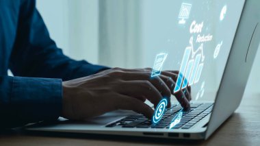 Hands typing on a laptop with visual graphs and icons projecting from the screen, representing business analytics and cost reduction strategy. Qubit.