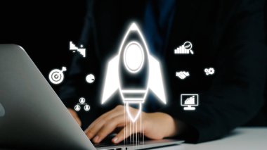 Bilgisayarda çalışan bir iş adamını gösteren parlak bir görüntü, dijital ortamda yenilik, başarı ve büyümeyi temsil eden bir roket sembolü ile birlikte. Dörtgen