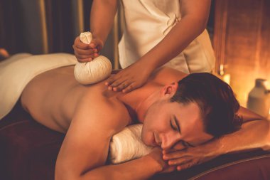 Sıcak bitkisel top spa masaj vücut tedavisi, masör erkek vücuduna nazikçe şifalı bitki torbası bastırıyor. Aromaterapi tesisinin sakinliği ve dinginliği kaplıca salonundaki mumların sıcacık ışığında. Sessiz.