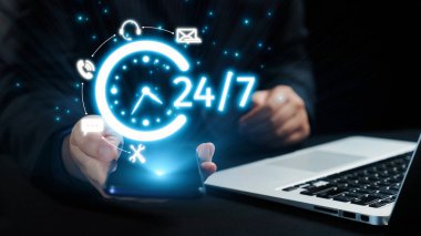 Bir dizüstü bilgisayarın yanında 24 saatlik servisi sembolize eden, profesyonel bir ortamda modern bağlantıyı ve ulaşılabilirliği gösteren akıllı telefonu gösteren canlı bir görüntü. Dörtgen
