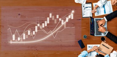 A business team collaborates on financial growth trends at a table. They utilize charts, graphs, and a laptop, emphasizing strategy and teamwork for success. Axiom