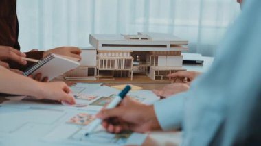 A diverse team is collaborating on an architectural project in a modern office, utilizing blueprints and a model to discuss ideas and strategies for a new design. SACTR
