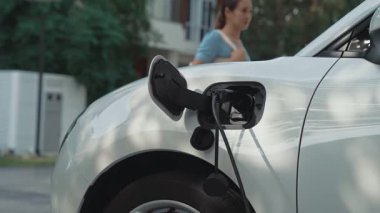 Bir kadın evinde elektrikli araç şarj aletinin fişini çekiyor. İlerici bir yaşam tarzında elektrikli araçların kullanımı, temiz ve sağlıklı bir çevreye katkıda bulunur..