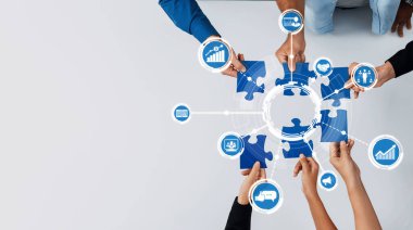 Hands arrange blue puzzle pieces with various business icons, symbolizing collaboration and strategy in a dynamic workplace focused on growth and innovation. Amity