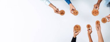 A top-down view of diverse hands engaged in teamwork, holding wooden gears that symbolize collaboration and innovation, emphasizing connection and shared goals. Amity
