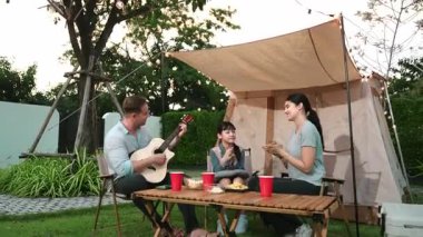 Baba gitar çalarken anne ve kız birlikte kampta oturuyorlar. Ebeveynler, genç nesil çapraz kuşak farklılıklarıyla zaman geçirmek için açık hava kamp aktivitelerini kullanıyorlar. Uyumsuzluk.
