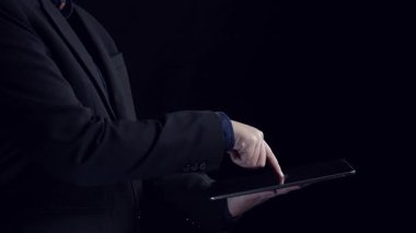 İş adamı, modern mali yönetimi ve vergilendirmenin iş dünyasındaki önemini simgeleyen, karanlık bir ortamda canlı dijital vergi simgelerini gösteren bir tablet sergiliyor. Dörtgen