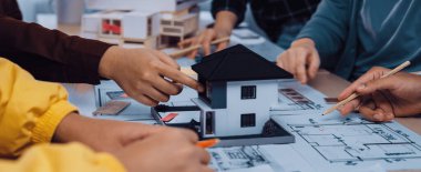 Çeşitli profesyonellerden oluşan bir grup, parlak ve modern bir çalışma alanında ayrıntılı ölçekli bir model ve planları inceleyen bir mimari tasarım projesi üzerinde işbirliği yapmaktadır. SACTR