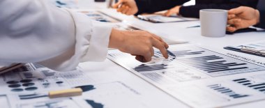 Bir masadaki grafik ve çizelgelere işaret eden, veri analizi ve profesyoneller arasındaki işbirlikçi tartışmaları vurgulayan dinamik bir iş toplantısı. SACTR