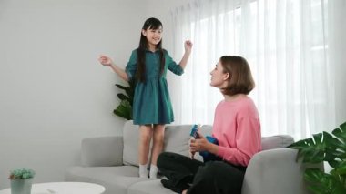 Annem gitar çalıp kıza bakarken yetenekli kız kanepede dans edip zıplıyor. Beyaz anne, çocuk oturma odasında dururken akustik müzik çalar. Aile eğlence konsepti. Pedagoji.