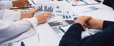 Bir iş ekibi, belgelerdeki çizelge ve grafikleri analiz etmek için bir toplantıda işbirliği yapıyor. Eller, profesyonel bir ortamda, takım çalışması ve veri güdümlü sezgilerin gösterilmesi gibi tartışmalara girişir. SACTR