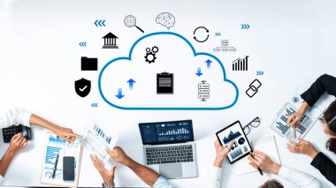 Professionals collaborate around a table using digital devices, discussing cloud technology while analyzing data through charts and graphs in a modern workspace. Trope