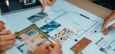 Çeşitli bireylerden oluşan bir grup detaylı bir mimari zemin planını inceliyor, düşünceli notlar ve minyatür bir modelle tasarım geliştirme alanları vurgulanıyor. SACTR