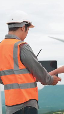 Erkek ve kadın mühendisler kırsal kesimdeki bir tepenin tepesinde ya da dağda rüzgar çiftliğinde çalışıyorlar. Yenilenebilir ve sürdürülebilir enerjinin gelecekteki üretimi için yenilikçi idealler.